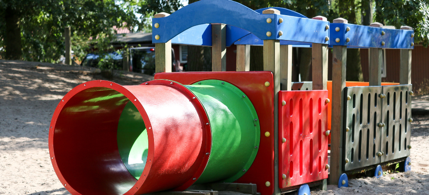 Eine bunte Holzeisenbahn steht auf einem Spielplatz im Sand.