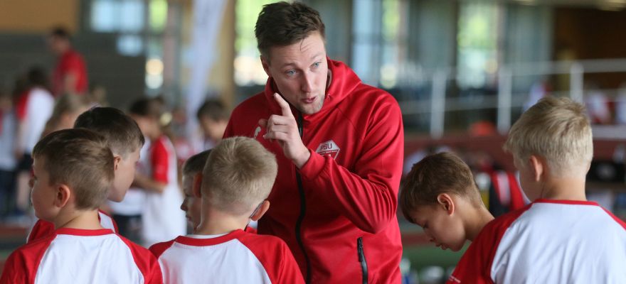 Mann mit roter Sportjacke erklärt Kindern die Regeln